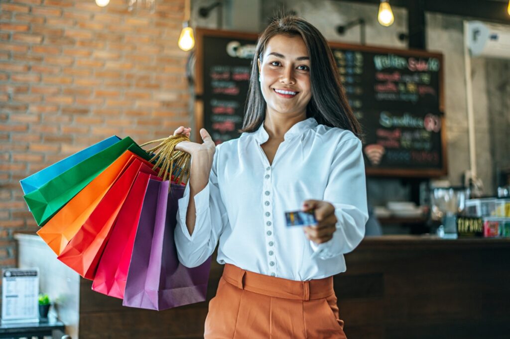 Mulher segurando sacolas de compras e cartão de crédito, simbolizando o uso responsável e os alertas do cartão de crédito.