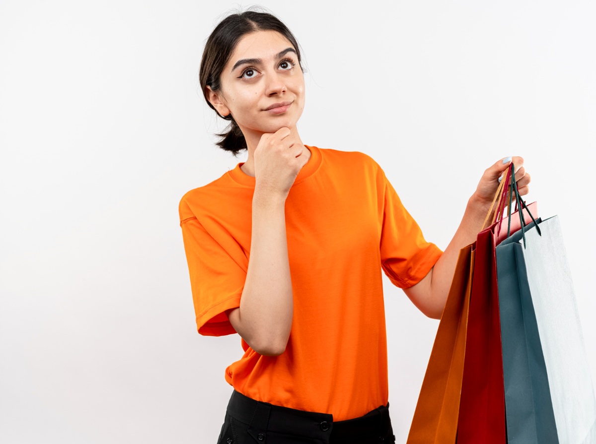 Mulher pensativa segurando sacolas de compras, representando a reflexão antes de compras por impulso.