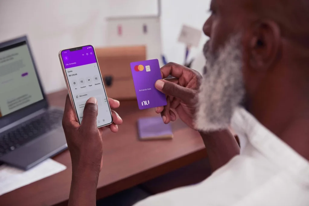 Homem usando o aplicativo do Nubank no celular, com cartão na mão.