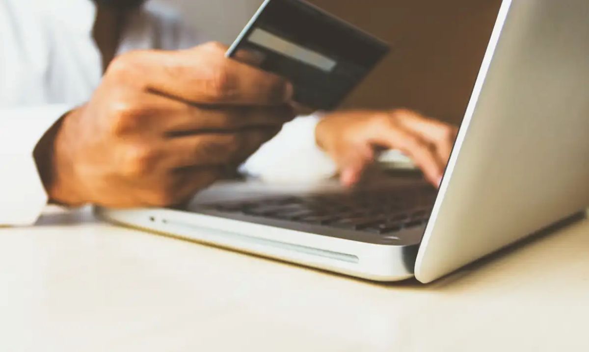 Pessoa segurando cartão de crédito enquanto usa notebook para fazer solicitação online