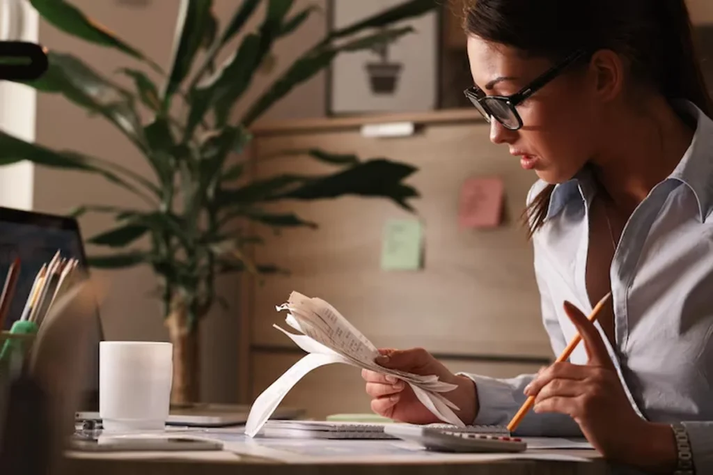 Mulher revisando documentos financeiros com calculadora e lápis, refletindo sobre planejamento financeiro.
