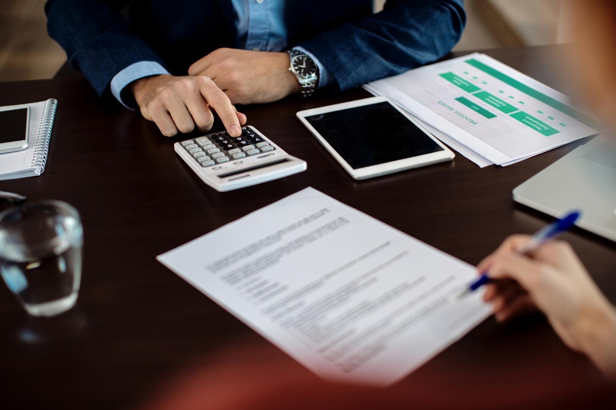 Duas pessoas analisando documentação financeira com calculadora e tablet em mesa de negociação revisando critérios de elegibilidade