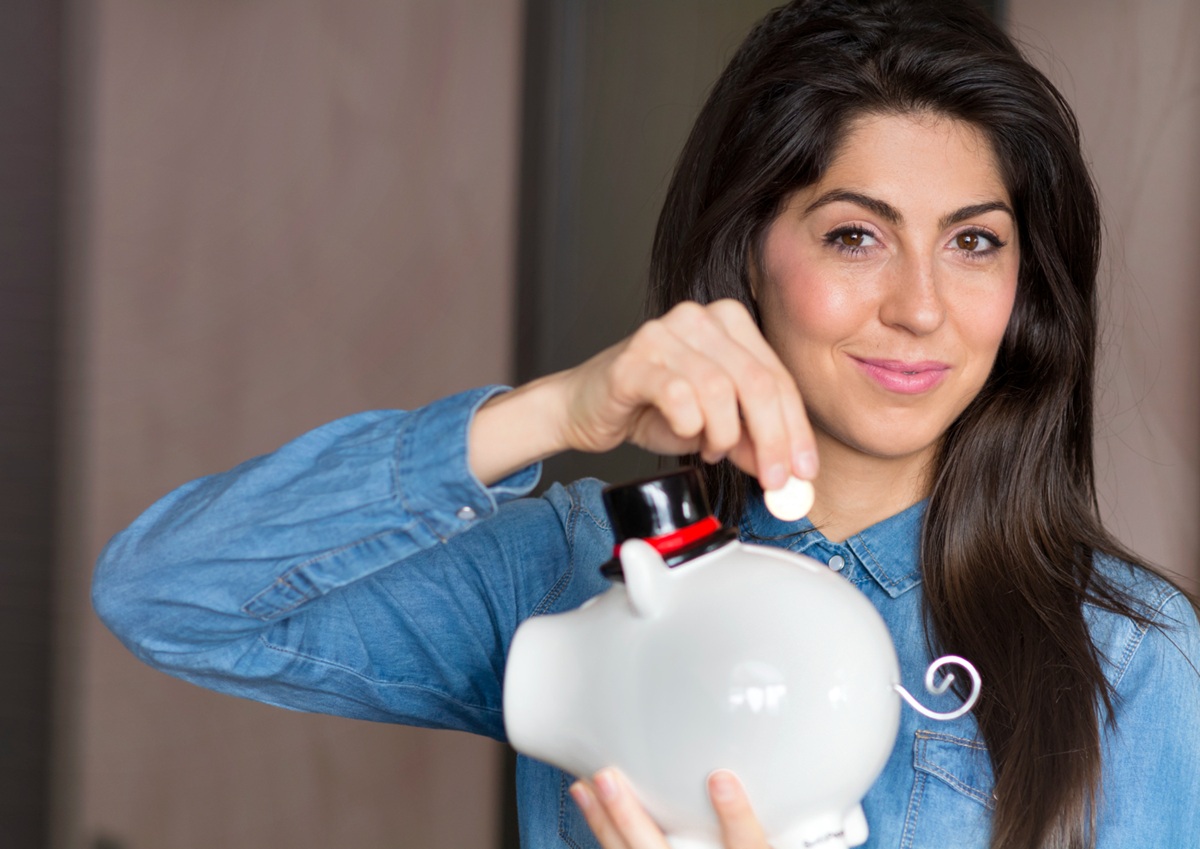 Mulher sorridente segurando cofrinho branco em formato de porco demonstrando método de organização financeira