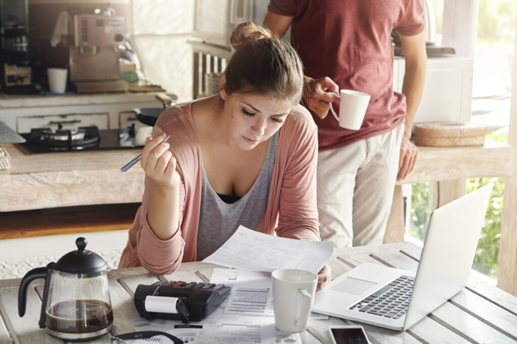Casal analisando contas e documentos financeiros em mesa com calculadora e notebook para planejamento mensal