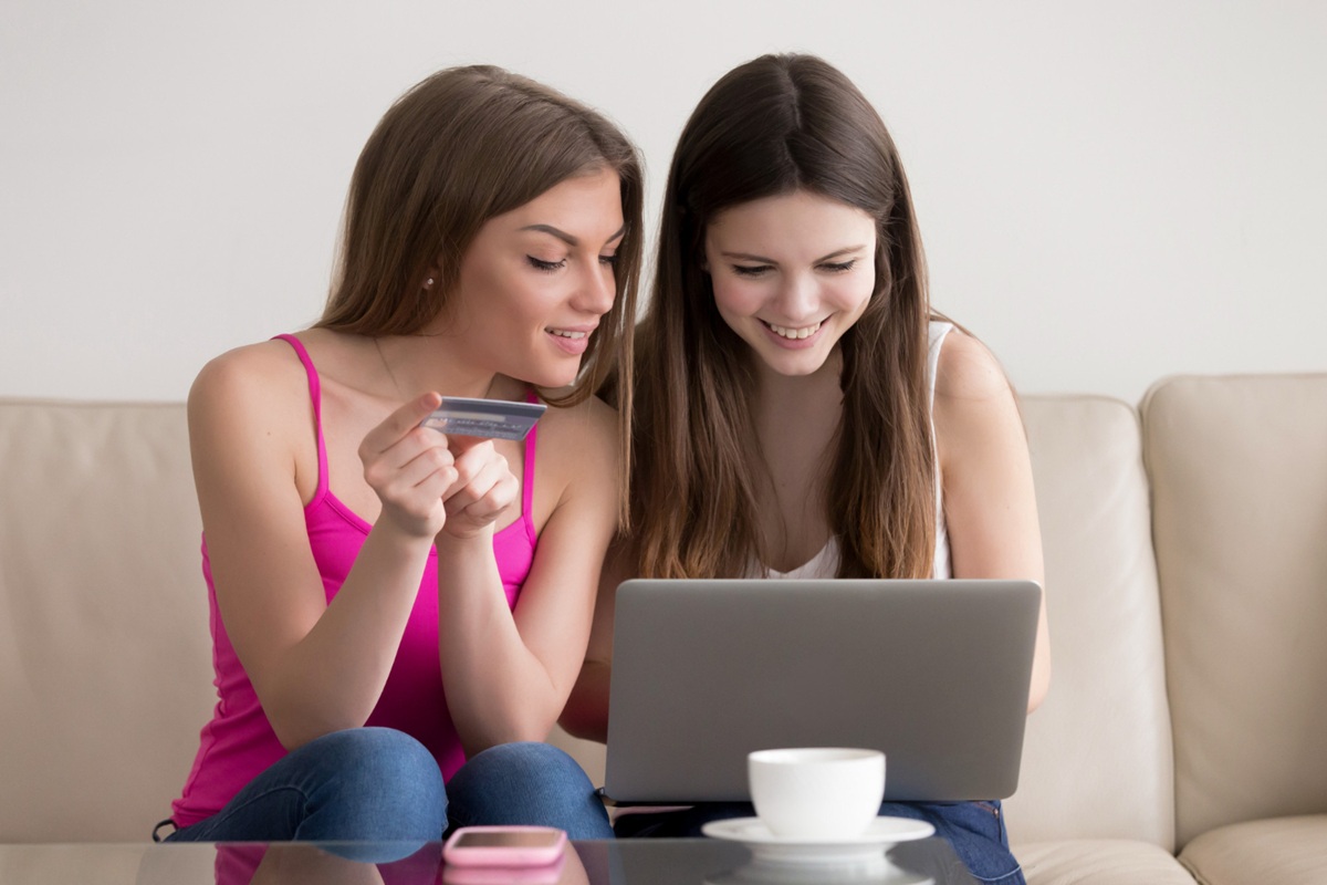 Duas amigas utilizando laptop e cartão de crédito para compras online com descontos