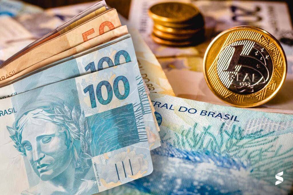 Salario mínimo representado por moedas e cédulas do real brasileiro, incluindo notas de 100 e 50 reais.
