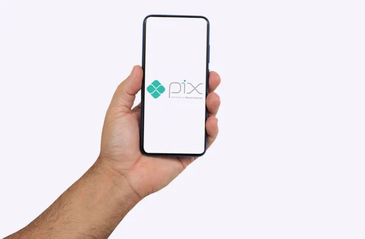 Mão segurando um celular com a tela inicial do Pix, indicando o acesso ao aplicativo bancário para iniciar a contestação de uma transação. 