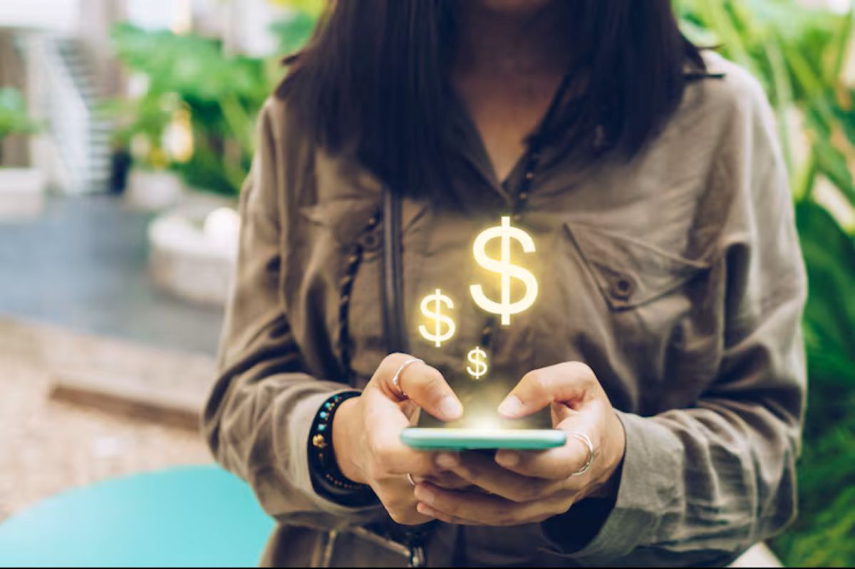 Mulher segurando celular com ícones de cifrão flutuando, representando economia digital.
