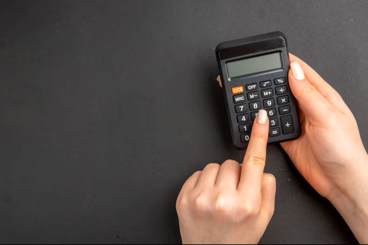 Mãos utilizando uma calculadora preta em fundo escuro, simbolizando o cálculo do Imposto de Renda progressivo e o imposto devido.