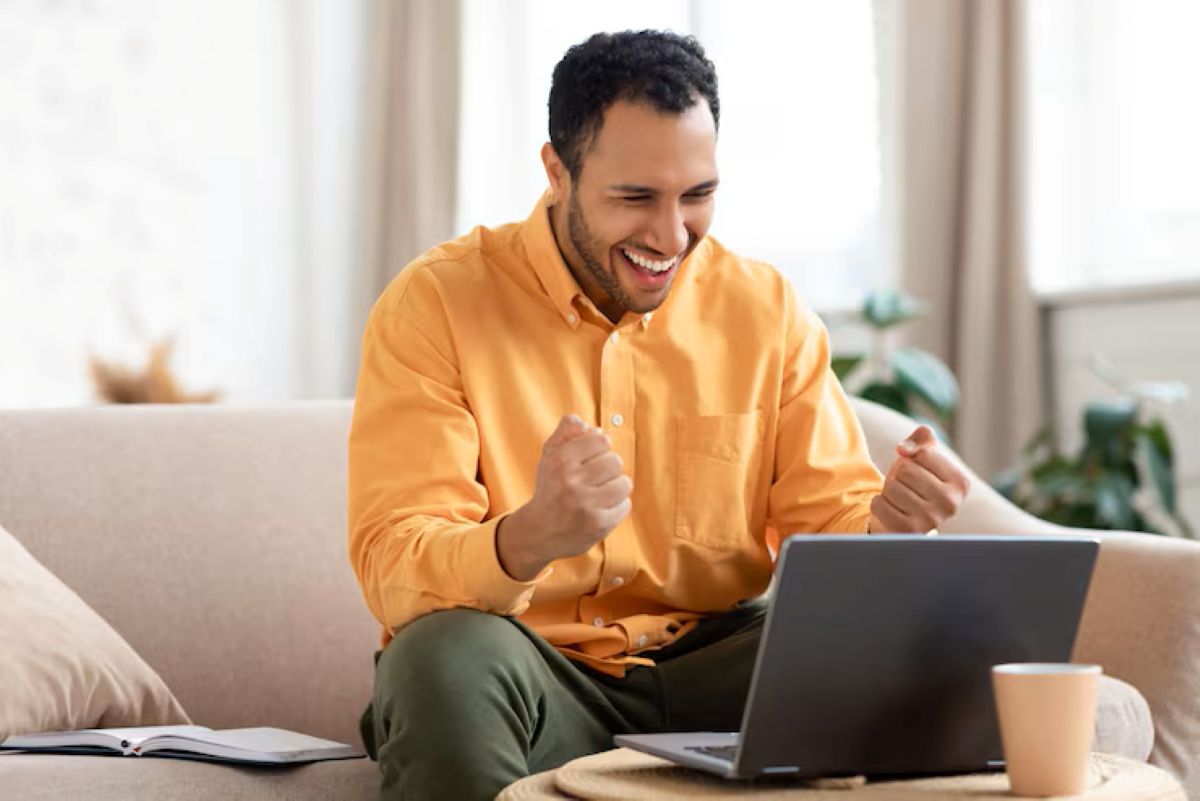 Homem sorrindo e comemorando no computador, representando a satisfação ao quitar dívidas no Serasa Limpa Nome