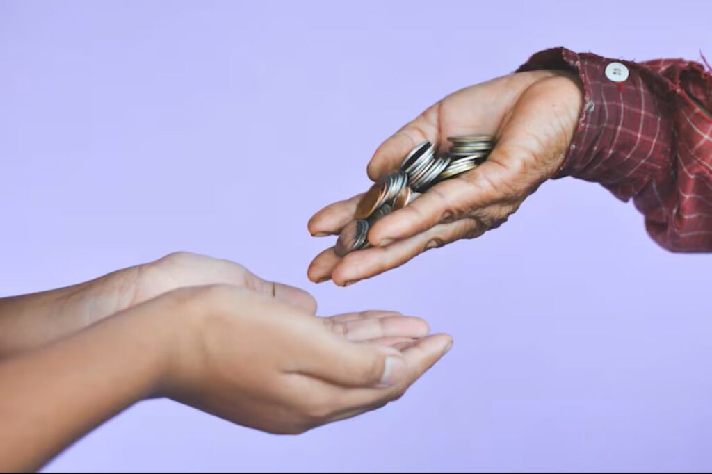 Mão de um adulto entregando moedas a uma criança como demonstração prática da mesada educativa