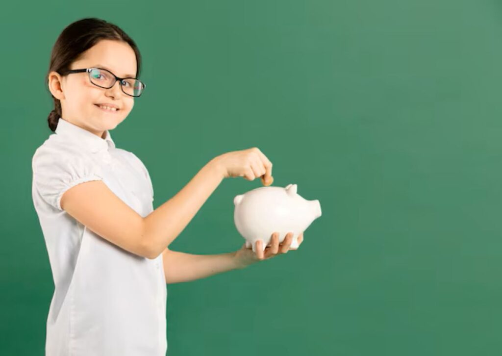 Menina sorridente de óculos colocando moeda em cofrinho de porco branco para ilustrar a educação financeira no Dia das Crianças.