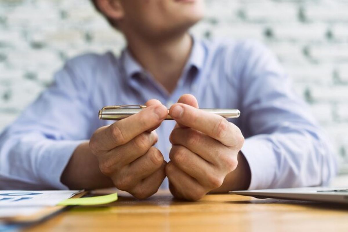 Mãos segurando uma caneta de metal em cima de uma mesa de escritório, com o foco em um sorriso ao fundo, simbolizando a tomada de decisão para a regularização de uma situação financeira.