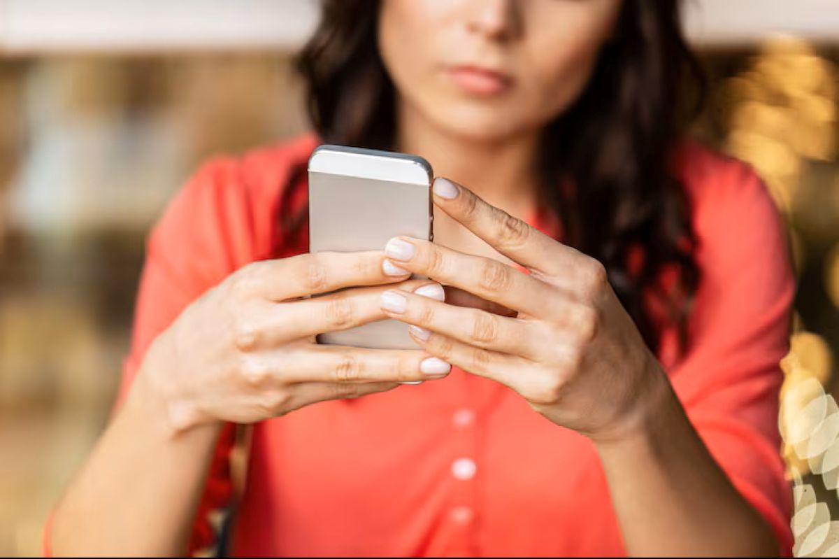 Mulher jovem com expressão séria, manuseando celular, representando a busca por soluções para problemas financeiros.