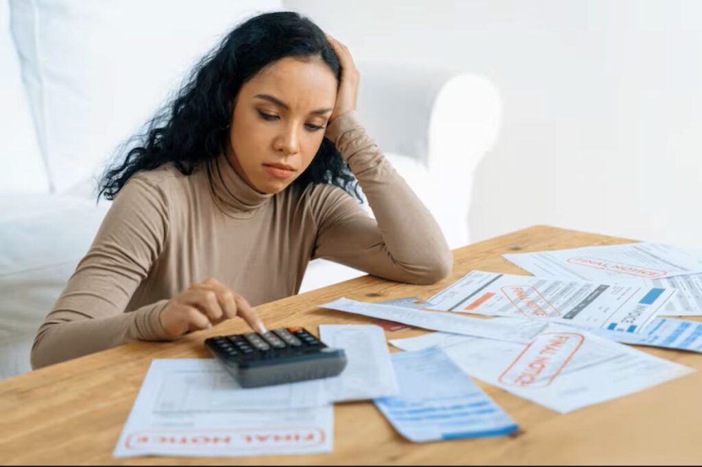 Mulher preocupada calculando em uma mesa cheia de contas e avisos de 'Final Notice', representando a seriedade do ajuizamento de dívida e suas consequências.