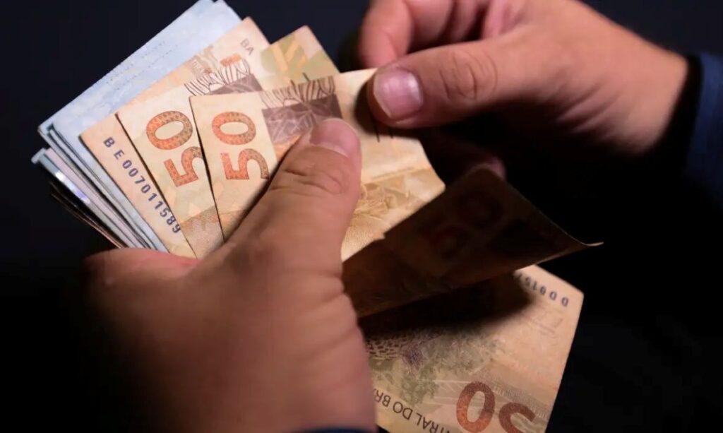 Mãos contando notas de cinquenta reais do Brasil sobre fundo preto