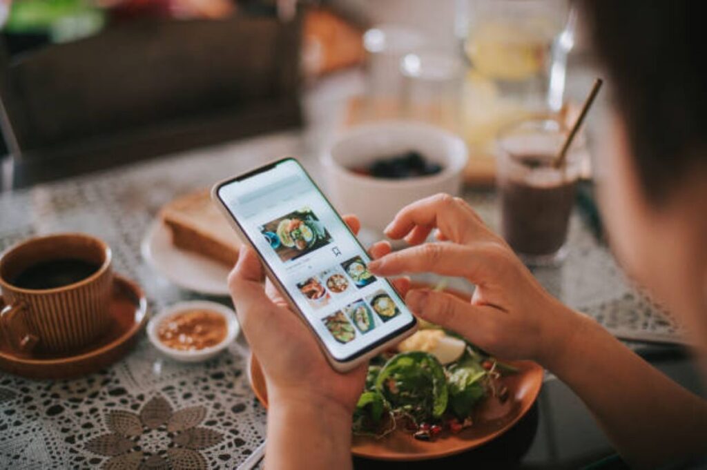 Pessoa consulta opções de refeições pelo celular enquanto almoça em casa