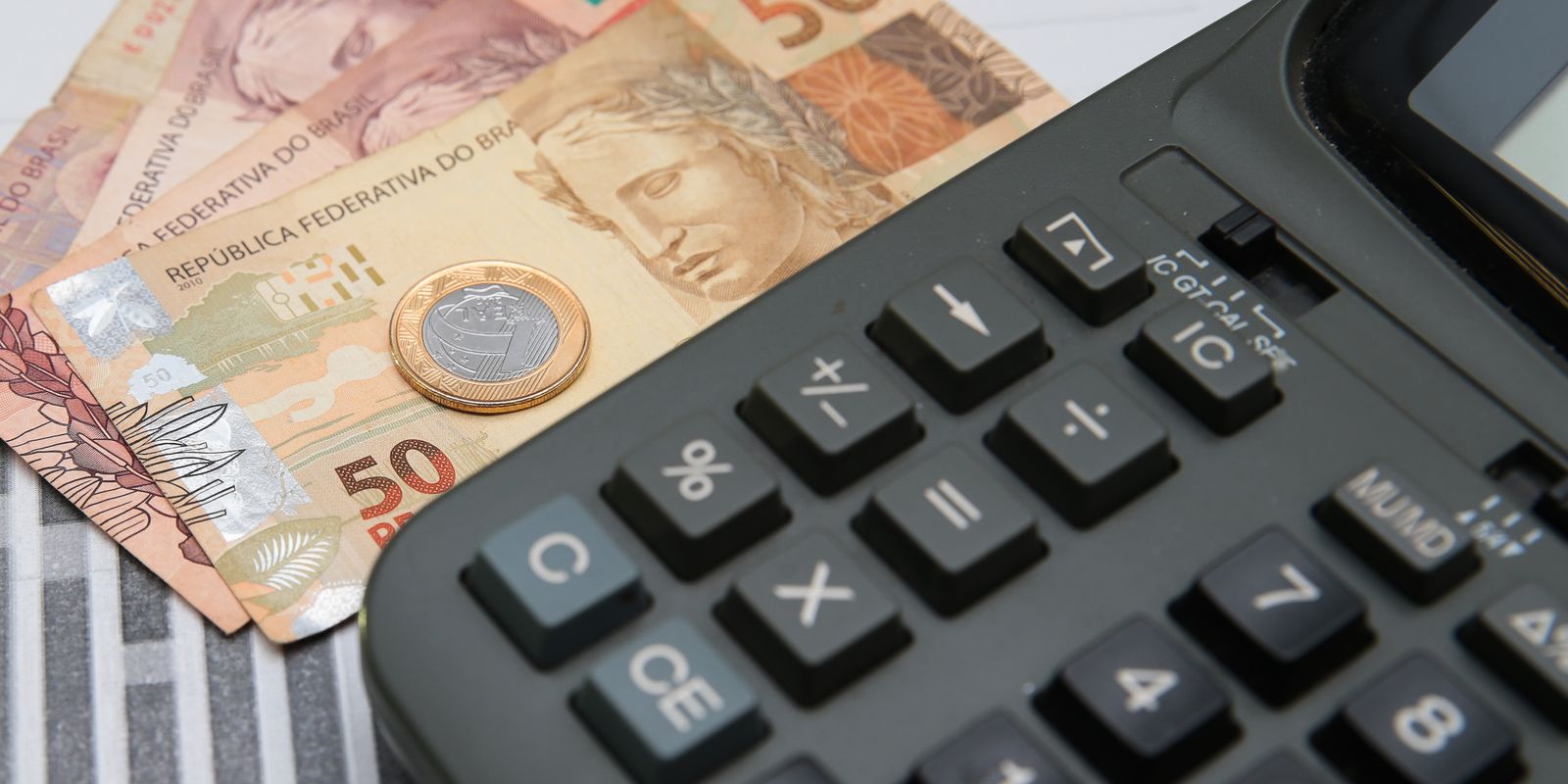 Notas de 50 reais, moeda de 1 real e calculadora preta representando cálculo financeiro
