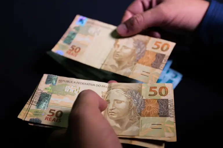 Mãos segurando e contando notas de cinquenta reais em fundo preto