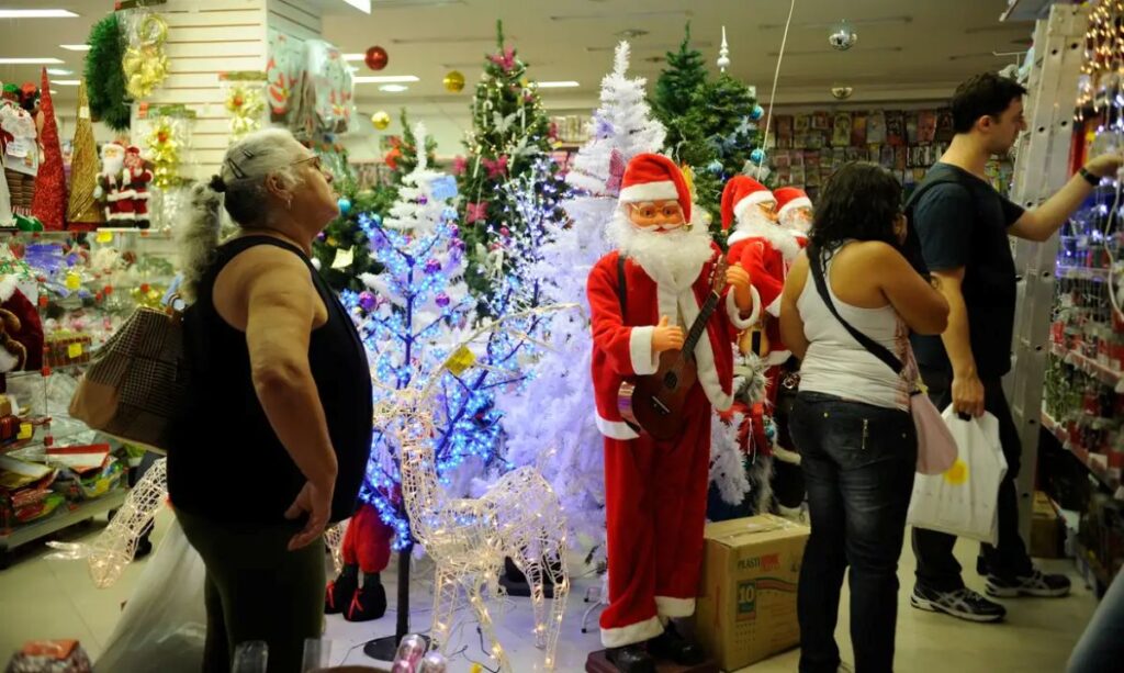 Pessoas observam objetos de Natal, árvores iluminadas e bonecos de Papai Noel em loja decorada