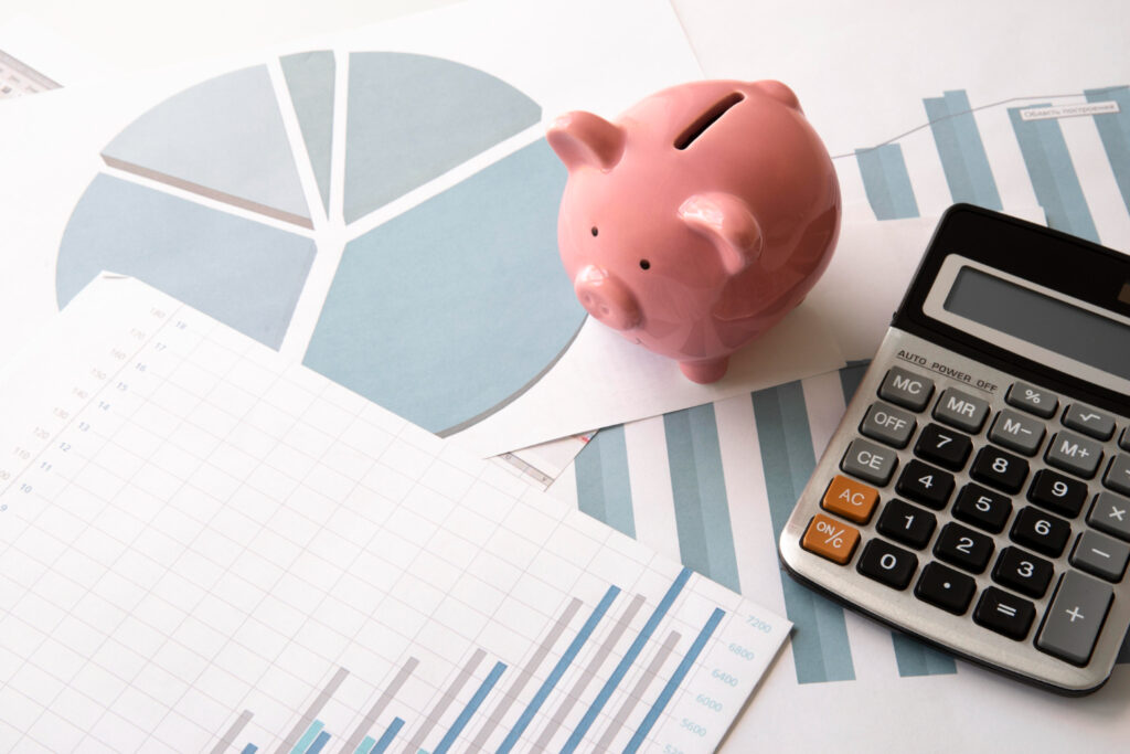 magem ilustrativa de cofre em formato de porquinho sobre gráficos financeiros ao lado de uma calculadora, representando o cálculo das fatias do método 50-30-20
