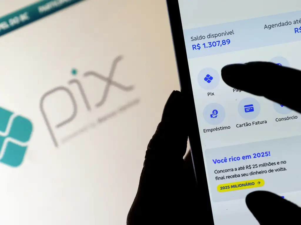Mão usando app bancário mostra saldo Pix de R$ 1.307,89 e aviso promocional amarelo
