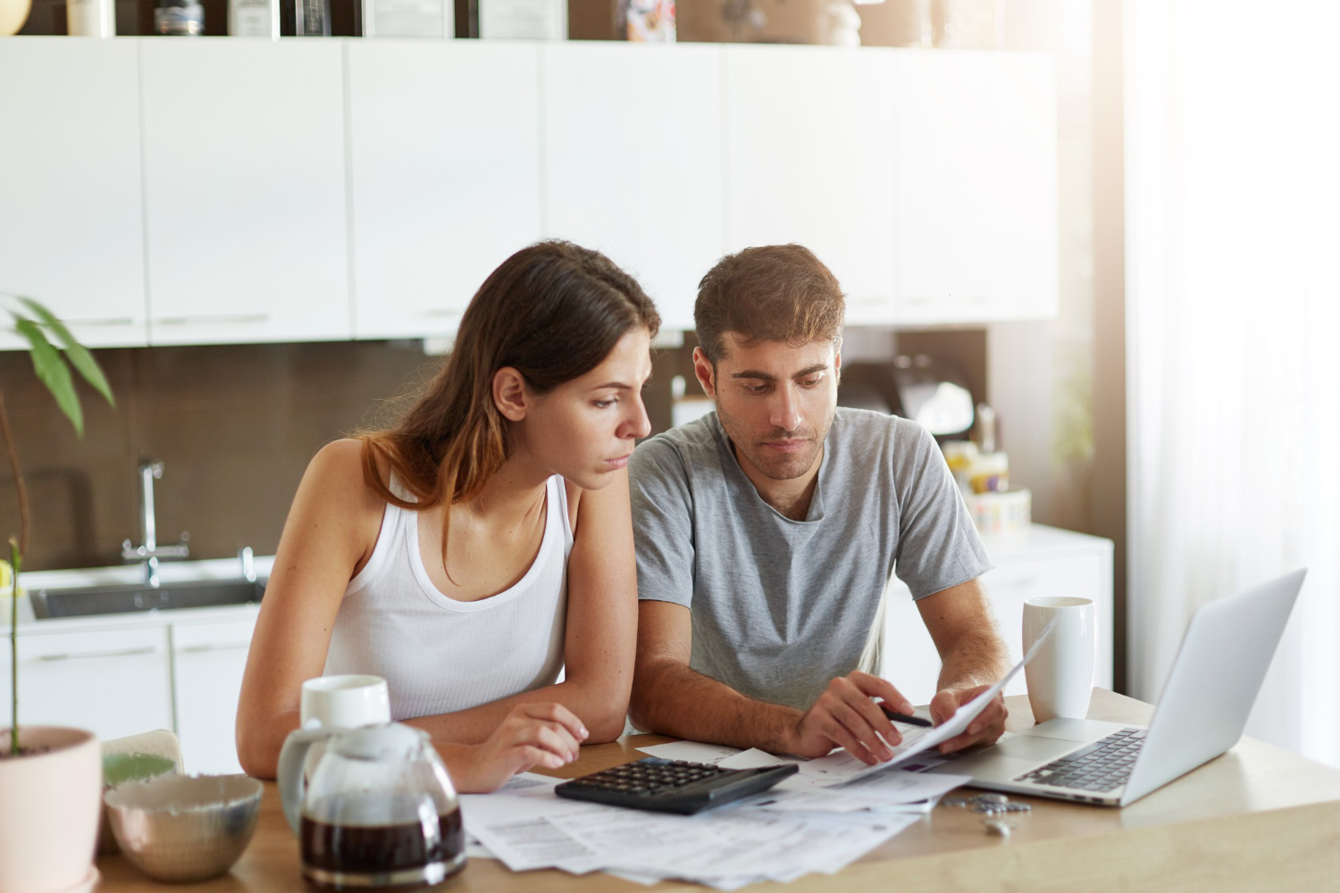 Imagem ilustrativa de casal reunido à mesa da cozinha analisando contas e usando calculadora, cena ligada ao diálogo sobre finanças na relação.