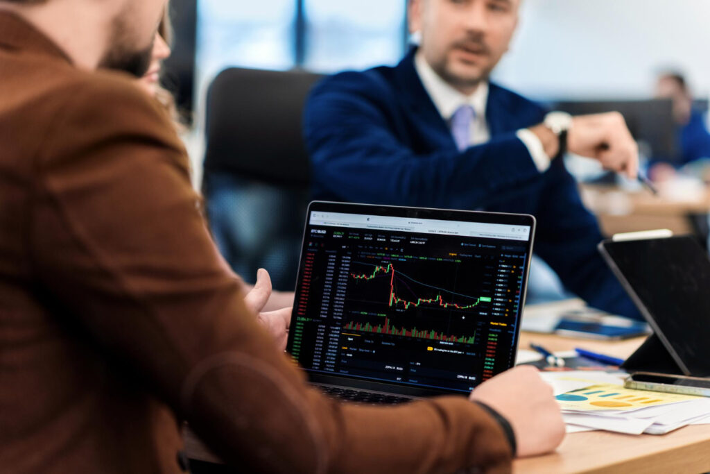Imagem ilustrativa de investidores observando gráficos financeiros na tela de um notebook durante reunião em escritório, em referência ao funcionamento do CDB pós-fixado