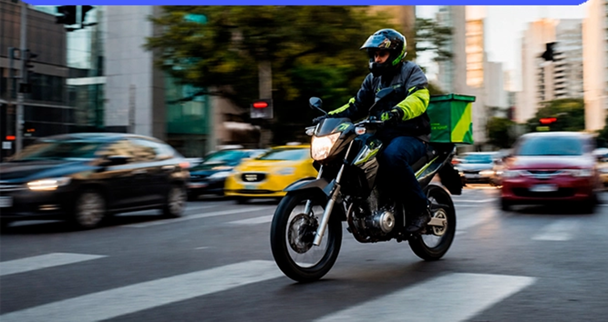 Imagem ilustrativa de entregador em uma motocicleta com baú trafegando em avenida movimentada, cena ligada aos profissionais que dependem do veículo para trabalhar.