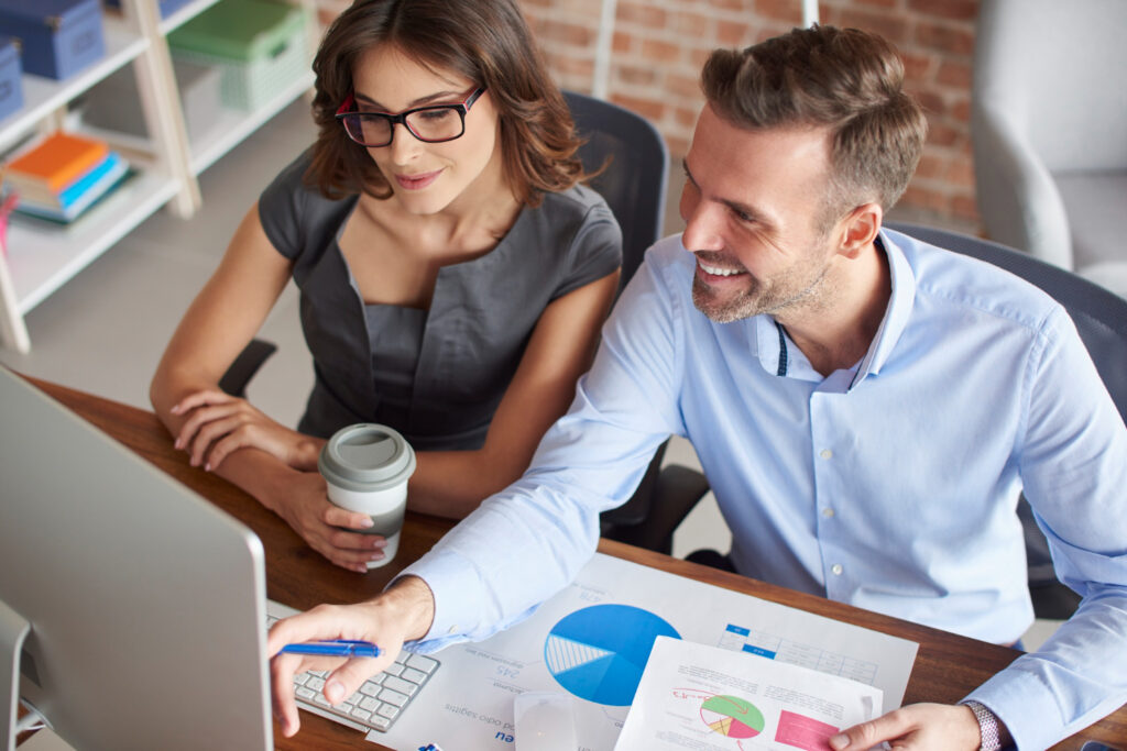 Imagem ilustrativa de dois profissionais analisando gráficos impressos e tela de computador em ambiente de escritório, em referência à organização do orçamento nas finanças pessoais e empresariais