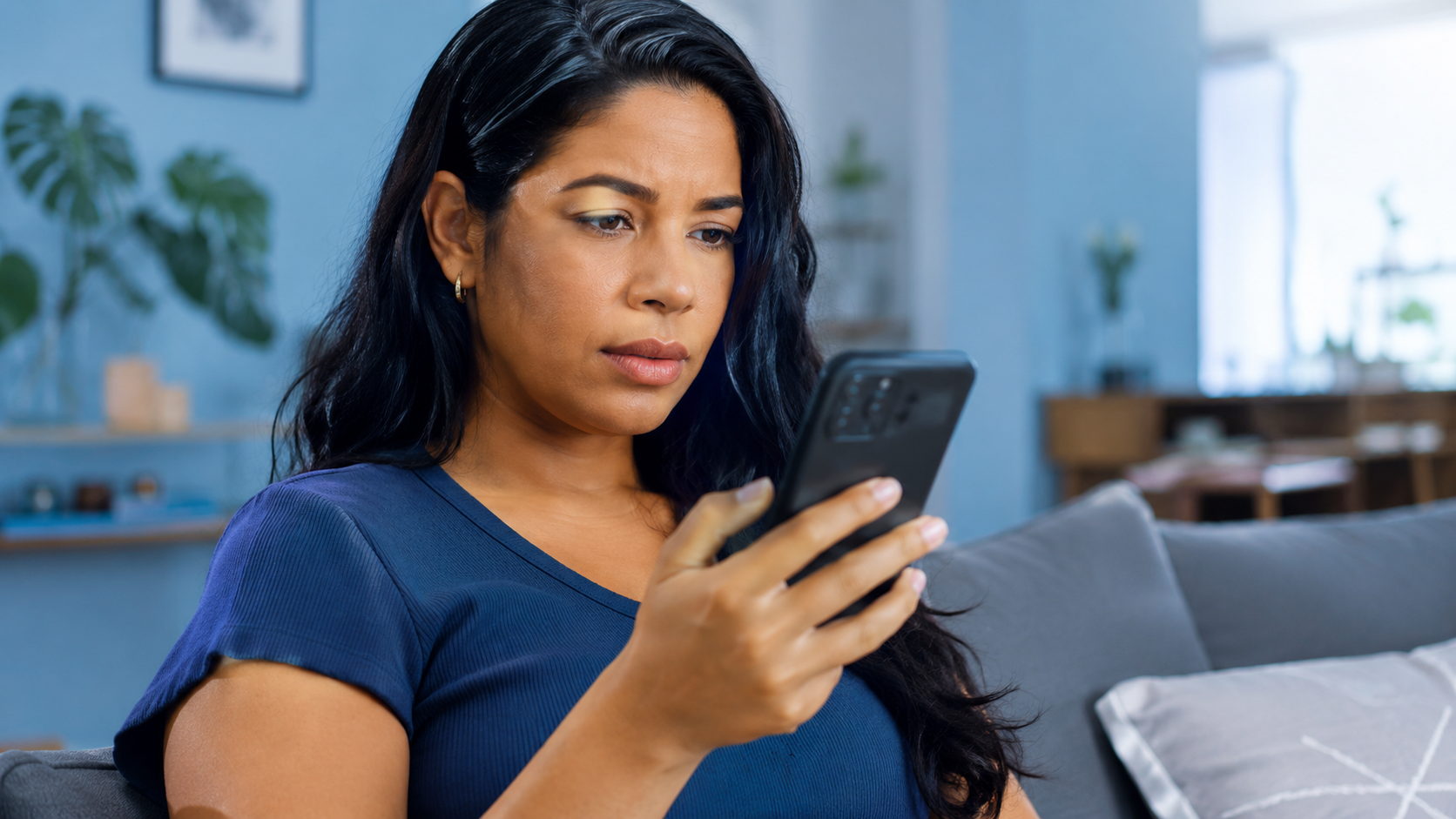 Imagem ilustrativa de mulher com expressão concentrada olhando o celular no sofá, representando o investidor que busca onde acompanhar seus títulos públicos