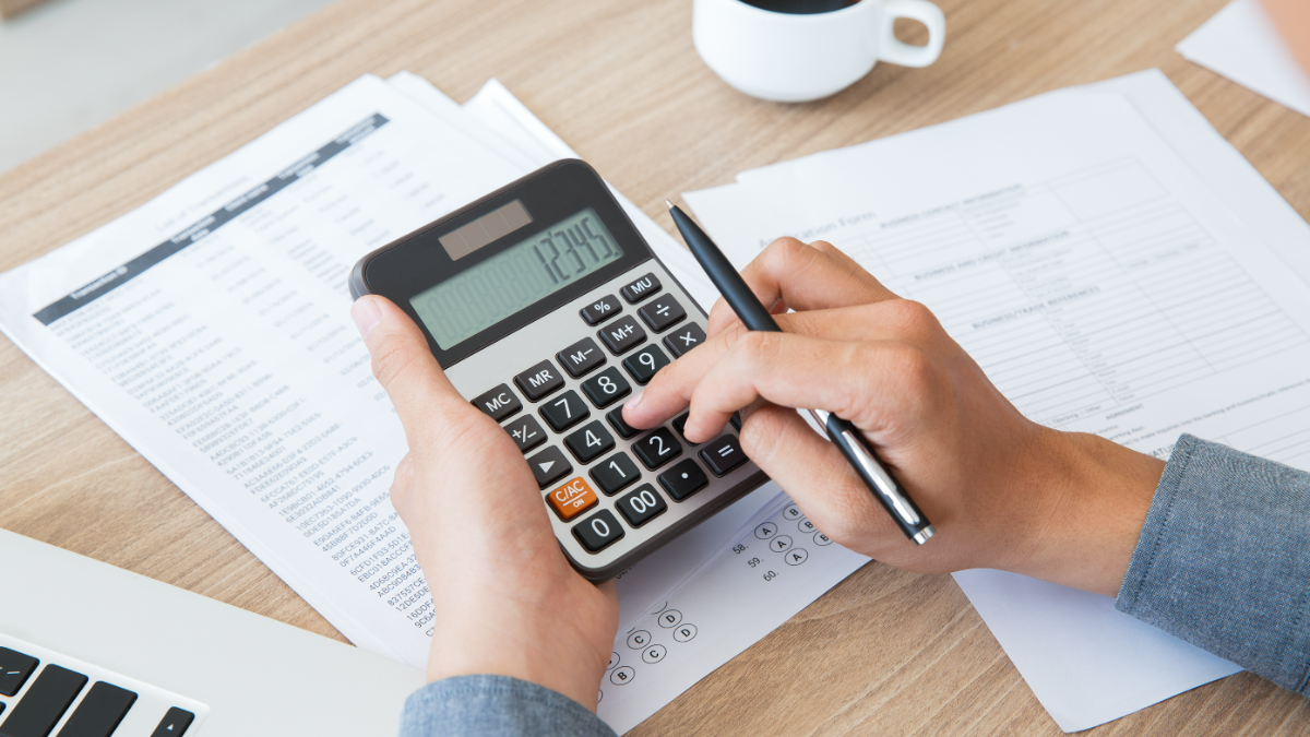 Homem calcula dados financeiros com calculadora e relatórios.