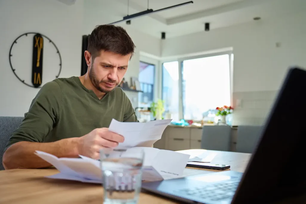 Homem analisa documentos de financiamento sentado à mesa, representando a decisão de antecipar parcelas da dívida.