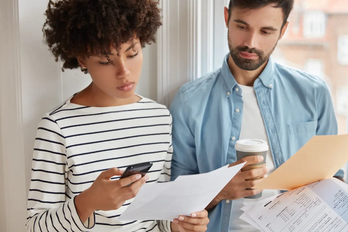 Casal analisa documentos de financiamento enquanto consulta informações no celular sobre antecipação de parcelas e redução de juros.