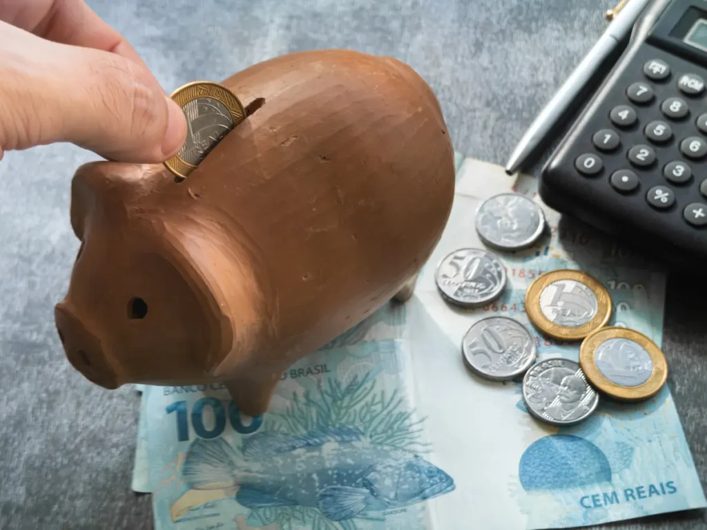 Cofrinho com moedas, notas de real e calculadora representando organização financeira.