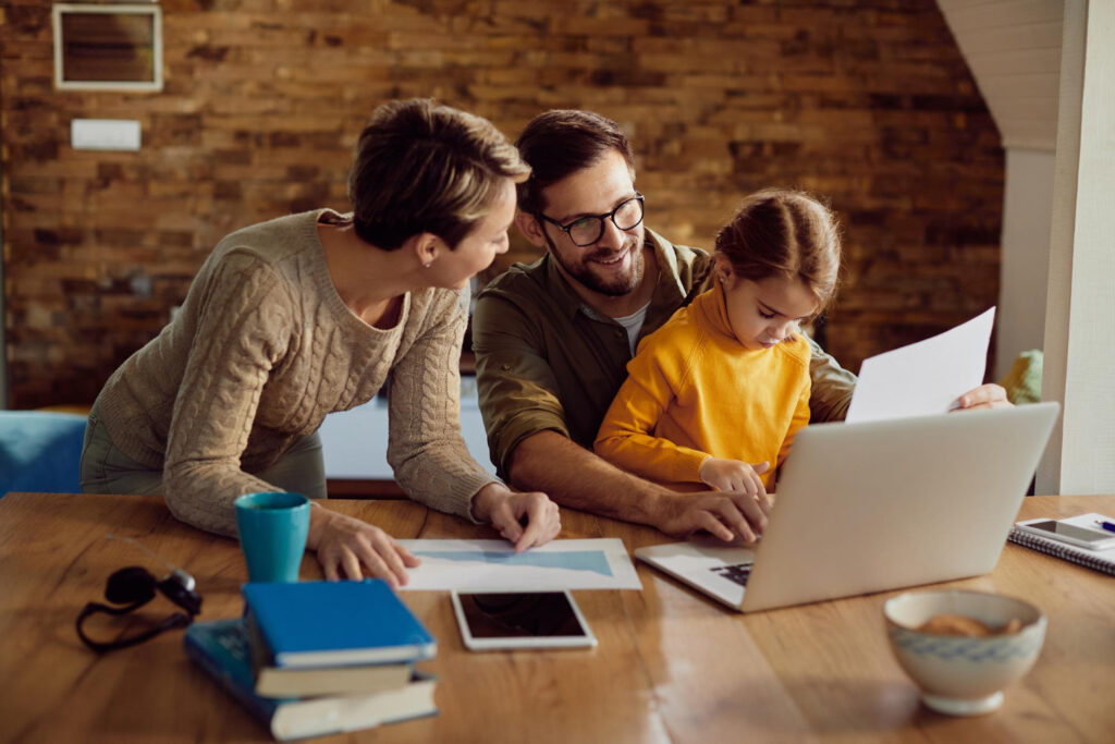 Imagem ilustrativa: casal e criança olham planilhas e notebook à mesa, cena ligada ao planejamento financeiro