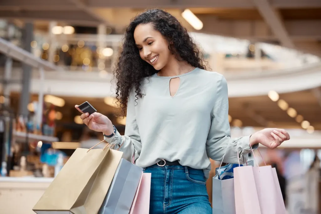Consumidora participa da Semana do Cliente em shopping com cartão de pagamento e sacolas de compras.