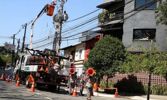 Imagem ilustrativa: equipe de eletricistas trabalha em poste de energia com caminhão e cones na rua, cena que remete às regras da Tarifa Social de Energia